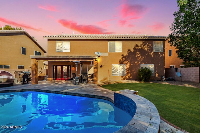 pool at dusk with a yard, ceiling fan, a patio area, and french doors