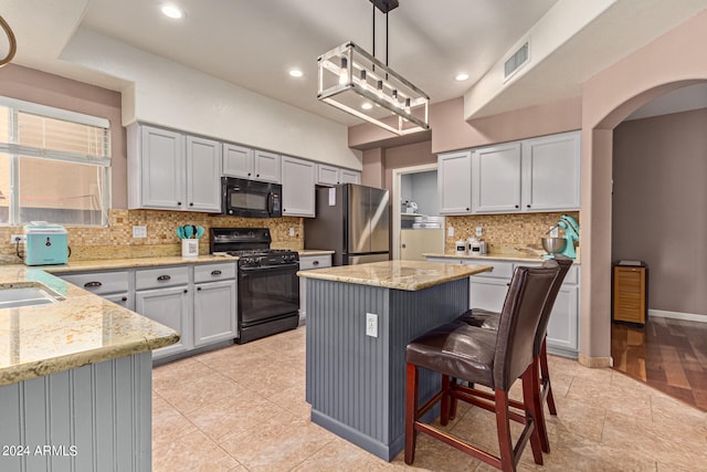 kitchen with decorative light fixtures, black appliances, a kitchen island, and tasteful backsplash