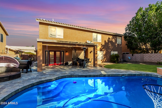 pool at dusk featuring ceiling fan and a patio area