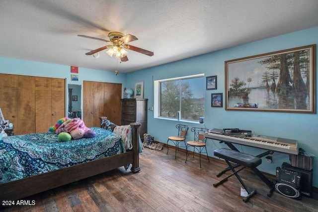 bedroom with a textured ceiling, two closets, dark hardwood / wood-style floors, and ceiling fan