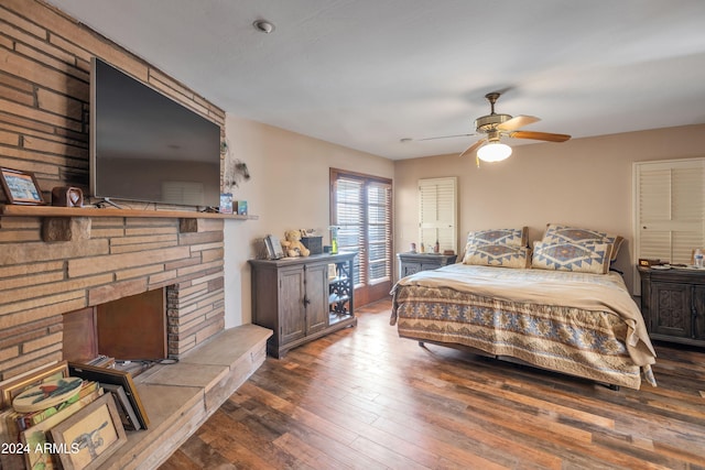 bedroom with a stone fireplace, dark hardwood / wood-style floors, and ceiling fan