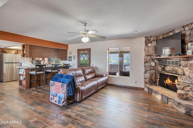 living room featuring ceiling fan, a textured ceiling, dark hardwood / wood-style flooring, and a fireplace