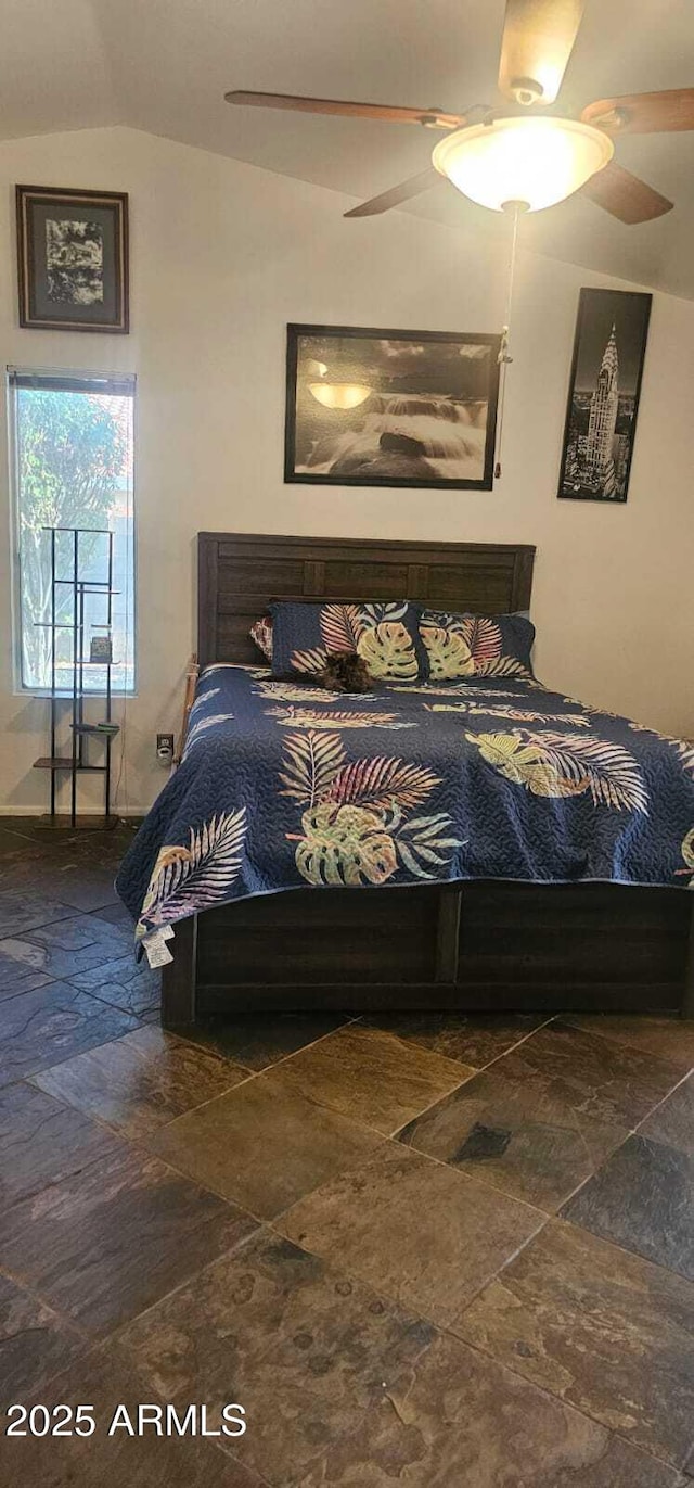 bedroom with ceiling fan, vaulted ceiling, and stone finish floor