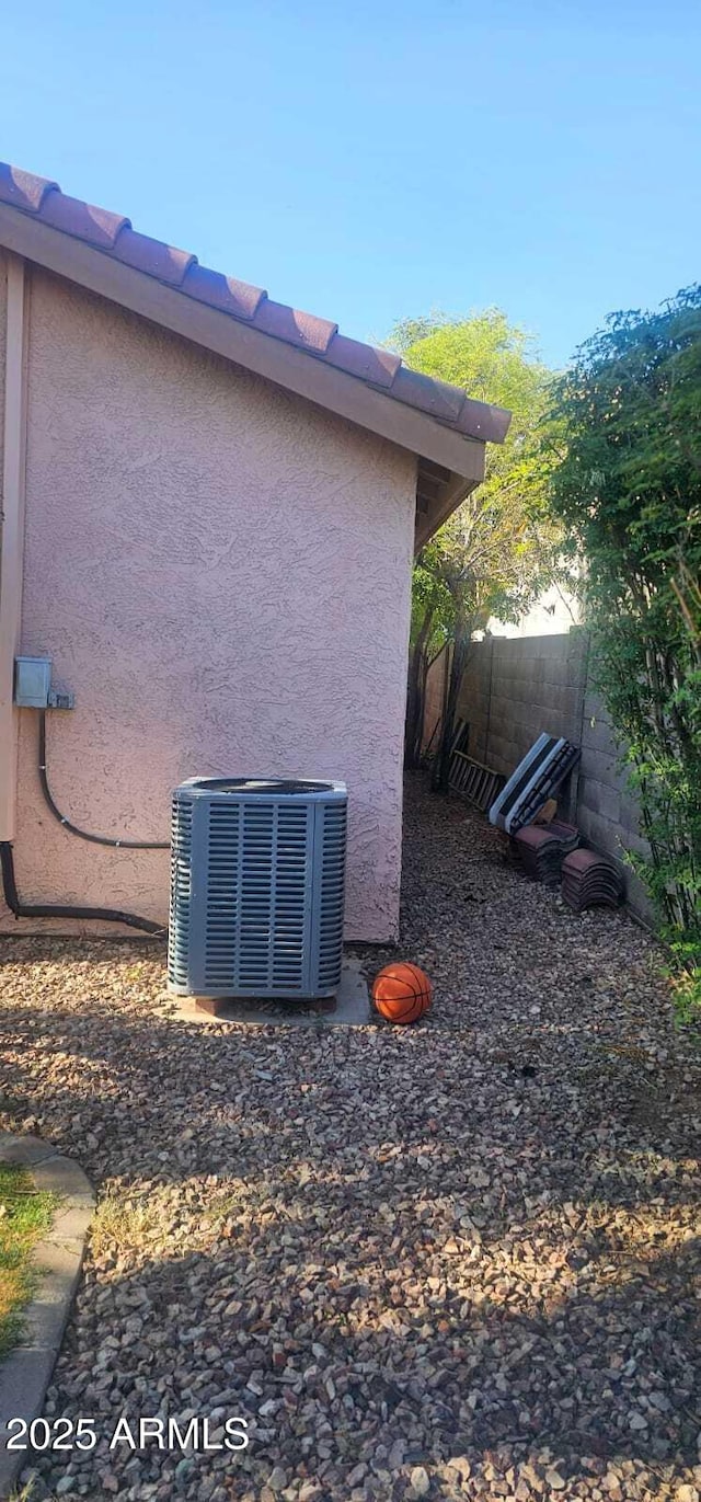view of side of property featuring fence, stucco siding, and cooling unit