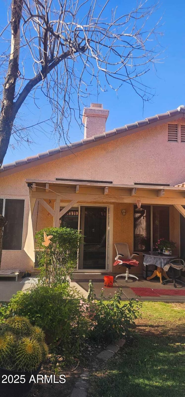 back of property featuring a patio, a chimney, and stucco siding