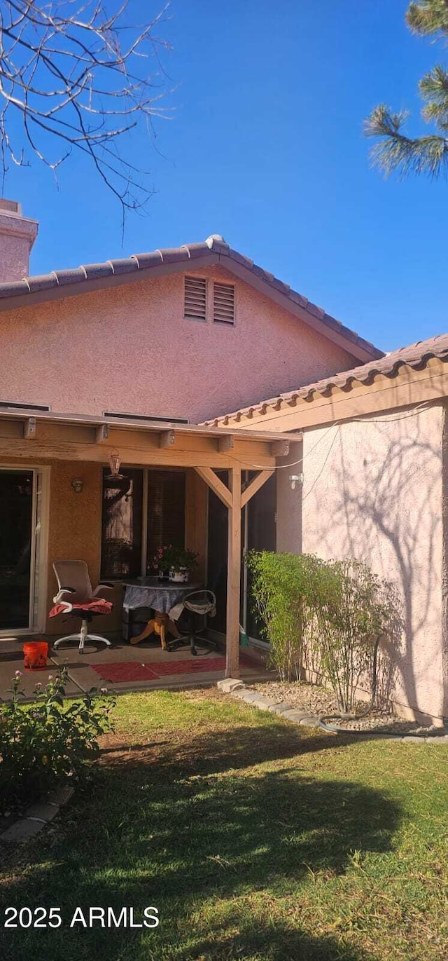 rear view of property featuring stucco siding, a yard, and a patio area