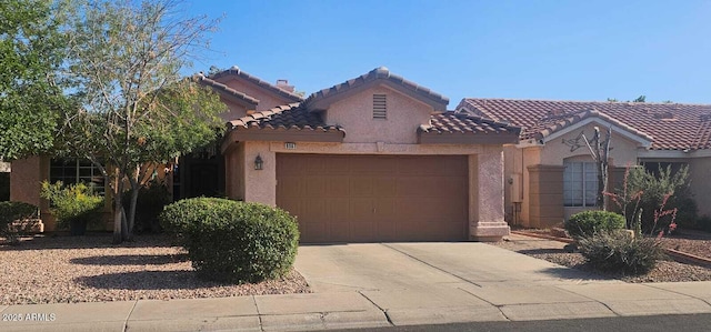 mediterranean / spanish house with a garage, stucco siding, driveway, and a tile roof
