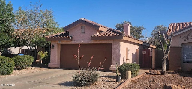 view of front of property with an attached garage, a tile roof, stucco siding, a chimney, and concrete driveway