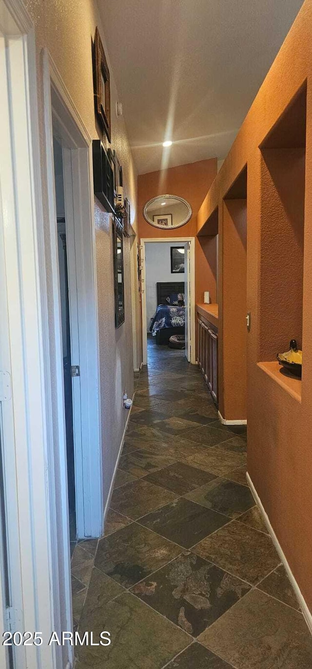 hallway featuring baseboards, stone finish floor, and visible vents