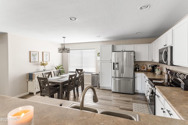 kitchen with light wood-style floors, white cabinets, recessed lighting, appliances with stainless steel finishes, and a sink