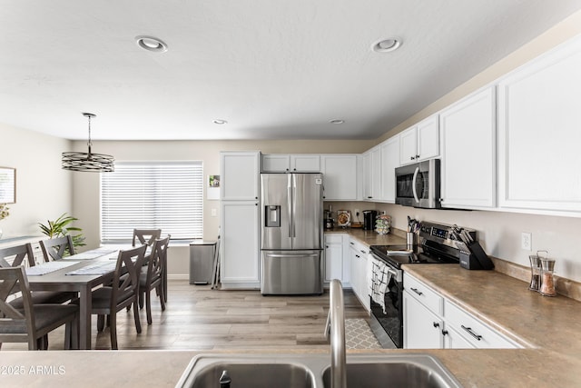 kitchen with hanging light fixtures, white cabinets, appliances with stainless steel finishes, recessed lighting, and light wood-style flooring