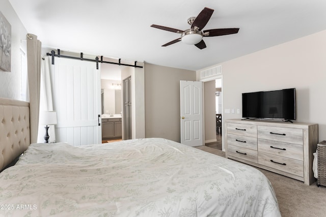 carpeted bedroom featuring visible vents, ceiling fan, connected bathroom, and a barn door