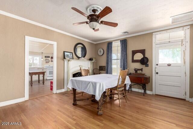 101 E Safford St, Tombstone, AZ 85638 - dining room with a fireplace, light wood-type flooring, a ceiling fan, baseboards, and ornamental molding