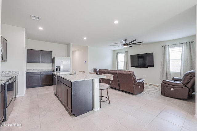 kitchen featuring sink, a breakfast bar area, a kitchen island with sink, stainless steel appliances, and dark brown cabinetry