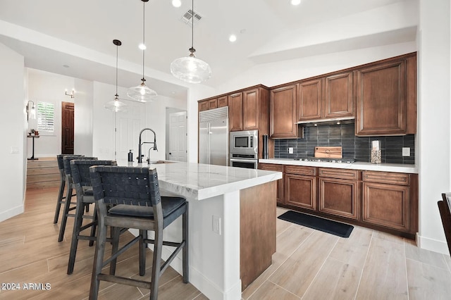 kitchen featuring sink, built in appliances, vaulted ceiling, hanging light fixtures, and a kitchen island with sink