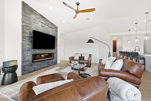 living room featuring light hardwood / wood-style flooring, a stone fireplace, lofted ceiling, ceiling fan, and sink