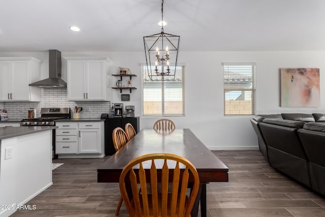 kitchen with wall chimney exhaust hood, tasteful backsplash, gas range, hanging light fixtures, and white cabinets