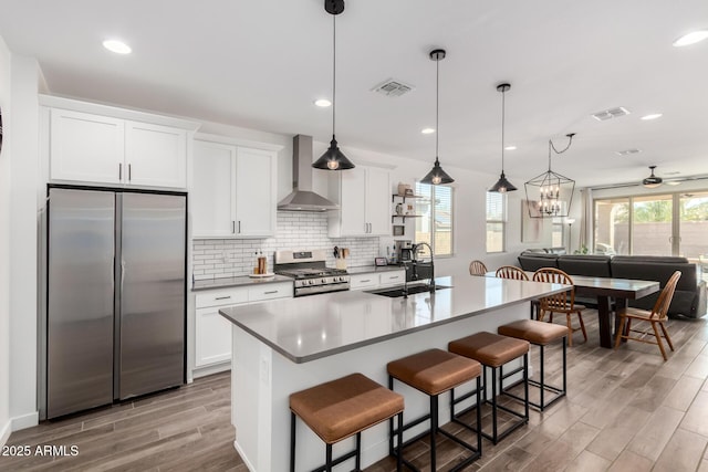 kitchen featuring wall chimney range hood, a kitchen breakfast bar, stainless steel appliances, a kitchen island with sink, and white cabinets