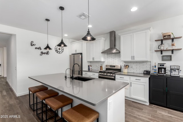 kitchen with appliances with stainless steel finishes, sink, an island with sink, and wall chimney range hood