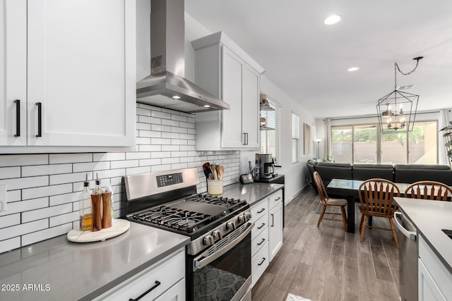 kitchen with pendant lighting, white cabinetry, stainless steel appliances, dark hardwood / wood-style floors, and wall chimney exhaust hood