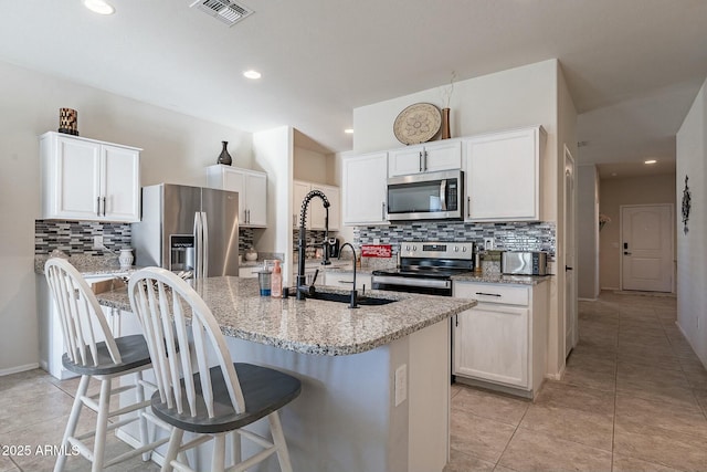 kitchen with white cabinetry, light stone counters, a kitchen bar, a kitchen island with sink, and appliances with stainless steel finishes