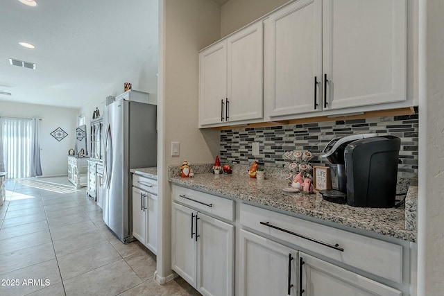 kitchen featuring backsplash, light stone counters, white cabinetry, stainless steel refrigerator, and light tile patterned flooring