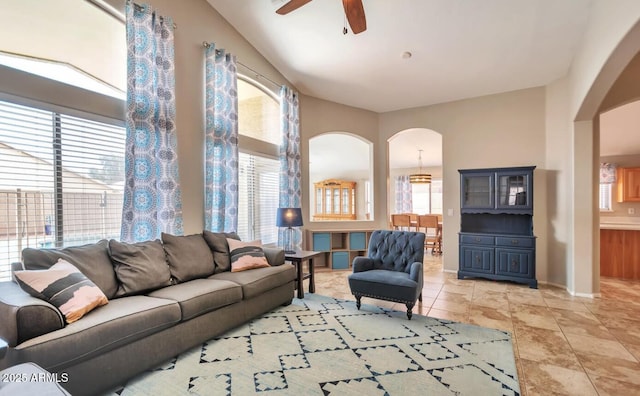 living area featuring light tile patterned floors, arched walkways, a ceiling fan, and baseboards