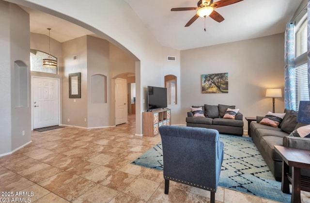 living room with arched walkways, baseboards, a ceiling fan, and a towering ceiling