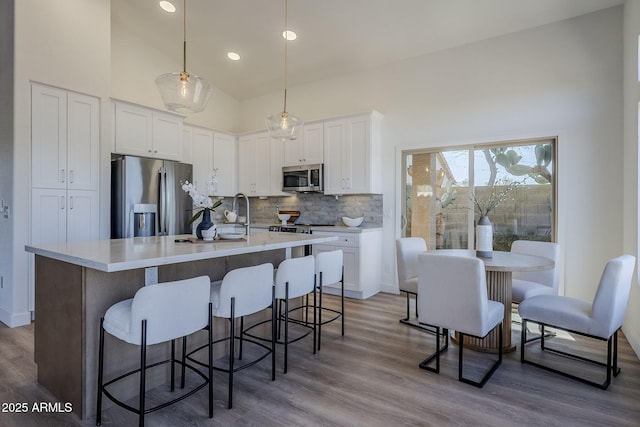 kitchen featuring tasteful backsplash, light countertops, appliances with stainless steel finishes, white cabinets, and high vaulted ceiling