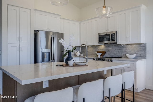 kitchen featuring appliances with stainless steel finishes, white cabinets, a center island with sink, and tasteful backsplash