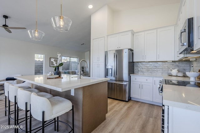 kitchen with light wood finished floors, appliances with stainless steel finishes, backsplash, and white cabinetry