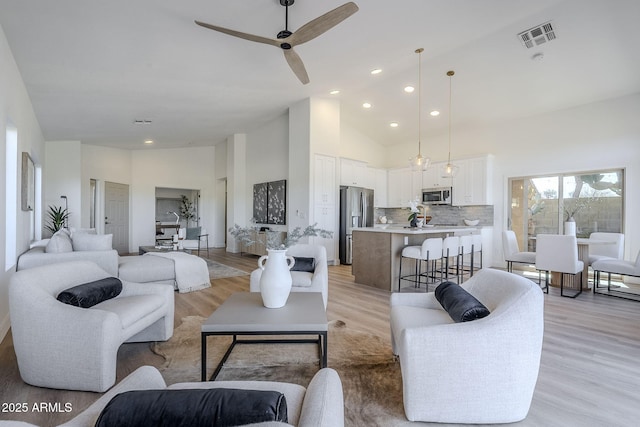 living room featuring light wood-style floors, visible vents, high vaulted ceiling, and recessed lighting