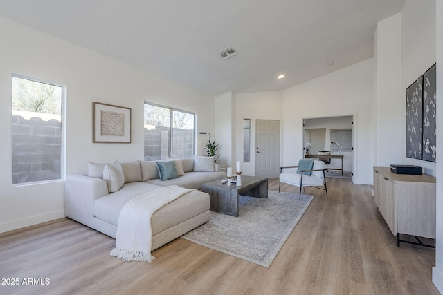 living area featuring high vaulted ceiling, light wood-type flooring, visible vents, and baseboards