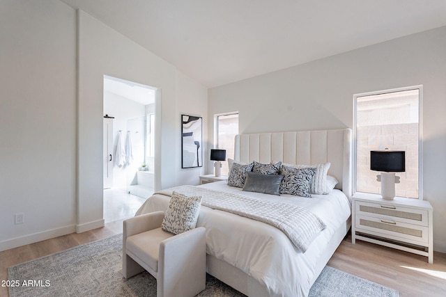 bedroom with baseboards, vaulted ceiling, wood finished floors, and ensuite bathroom