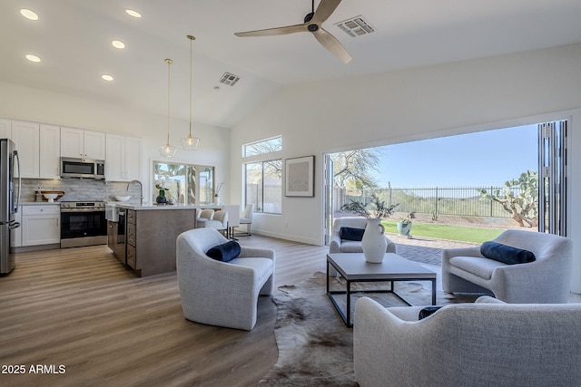 living room with high vaulted ceiling, a ceiling fan, visible vents, and wood finished floors