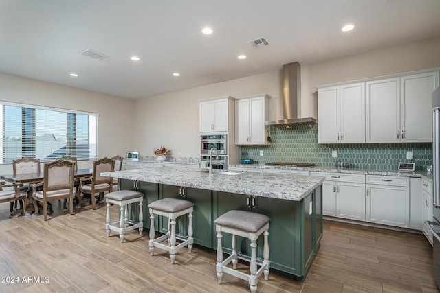 kitchen with a center island with sink, white cabinetry, wall chimney range hood, and a breakfast bar area