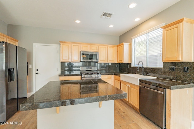 kitchen featuring a kitchen island, appliances with stainless steel finishes, light brown cabinetry, sink, and a kitchen bar