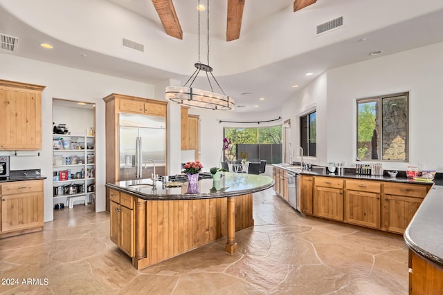 kitchen featuring stainless steel appliances, sink, beamed ceiling, hanging light fixtures, and an island with sink