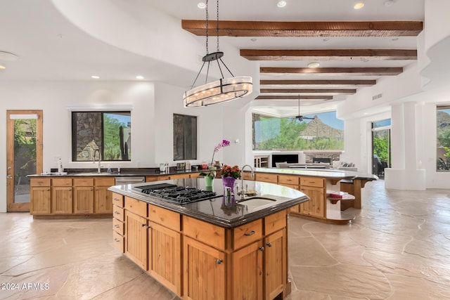 kitchen featuring hanging light fixtures, sink, an island with sink, beamed ceiling, and stainless steel gas cooktop