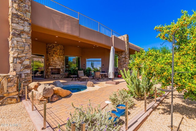 exterior space featuring an in ground hot tub, an outdoor stone fireplace, and a balcony