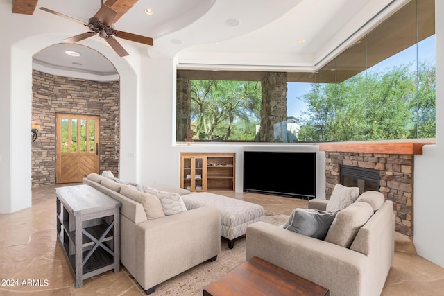 living room featuring ceiling fan, a stone fireplace, and a raised ceiling