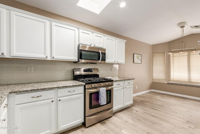 kitchen with white cabinets, stainless steel appliances, light stone counters, and light hardwood / wood-style floors