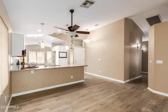 kitchen with white cabinets, kitchen peninsula, light stone counters, and light hardwood / wood-style floors