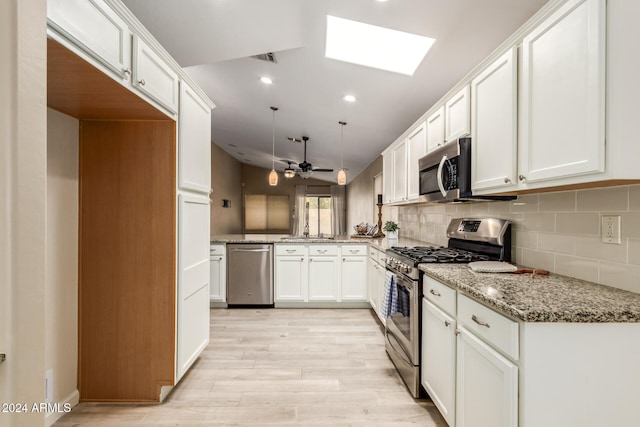 kitchen with white cabinetry, ceiling fan, hanging light fixtures, vaulted ceiling with skylight, and appliances with stainless steel finishes