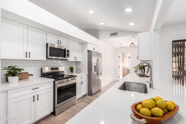 kitchen with stainless steel appliances, backsplash, vaulted ceiling, white cabinets, and sink