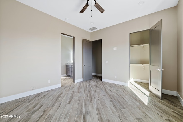 unfurnished bedroom featuring light wood-type flooring, ceiling fan, ensuite bathroom, a walk in closet, and a closet