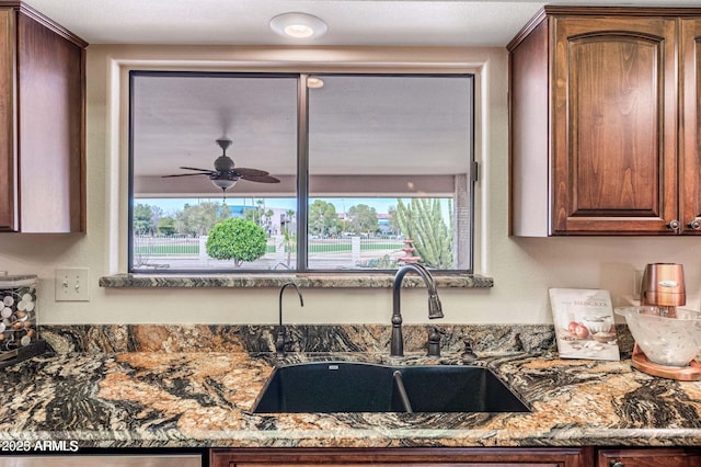 kitchen featuring ceiling fan, dark stone counters, and a sink