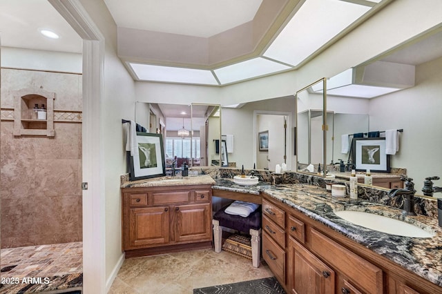 bathroom featuring a sink, tiled shower, two vanities, and a skylight