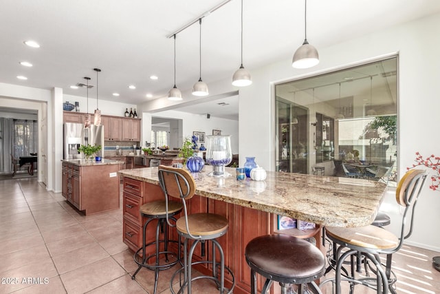 14363 W Acapulco Ln, Surprise, AZ 85379 - kitchen featuring a kitchen bar, light tile patterned floors, stainless steel fridge with ice dispenser, a kitchen island, and brown cabinetry