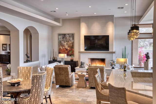 dining room with visible vents, recessed lighting, arched walkways, stone finish floor, and a large fireplace